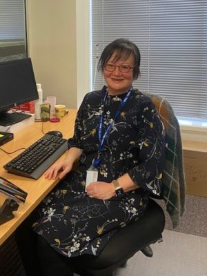 A smiling person sitting at an office desk 